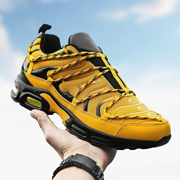 Yellow youth sports Korean fashion casual shoe with black accents and rubber sole held against sky background