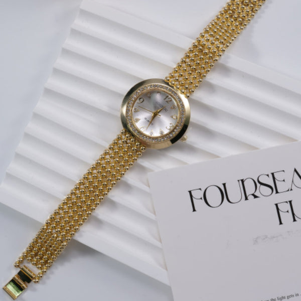 Women's Calendar Quartz sports watch with round dial and gold alloy mesh strap on white surface next to a paper sheet